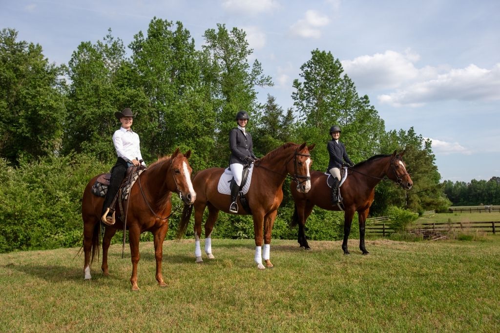 3 equestrians with their horses posing for a photo outside