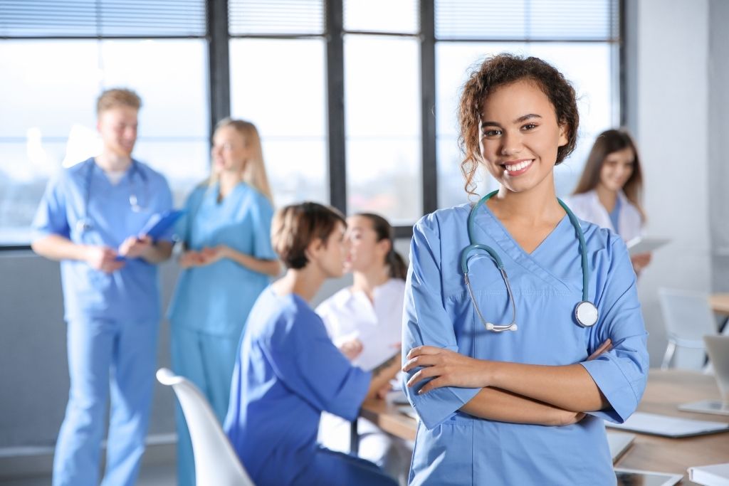 A BSN nursing student wearing blue scrubs stands in front of other students