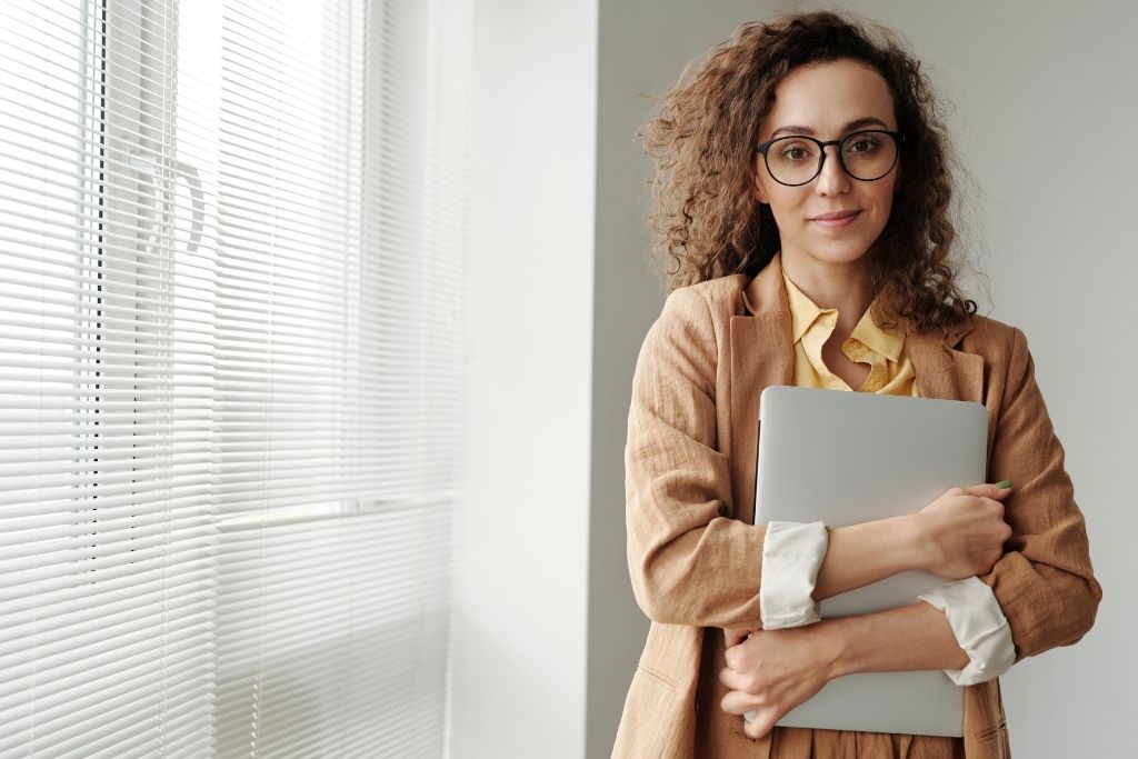 A female psychology student holds a laptop next to a window