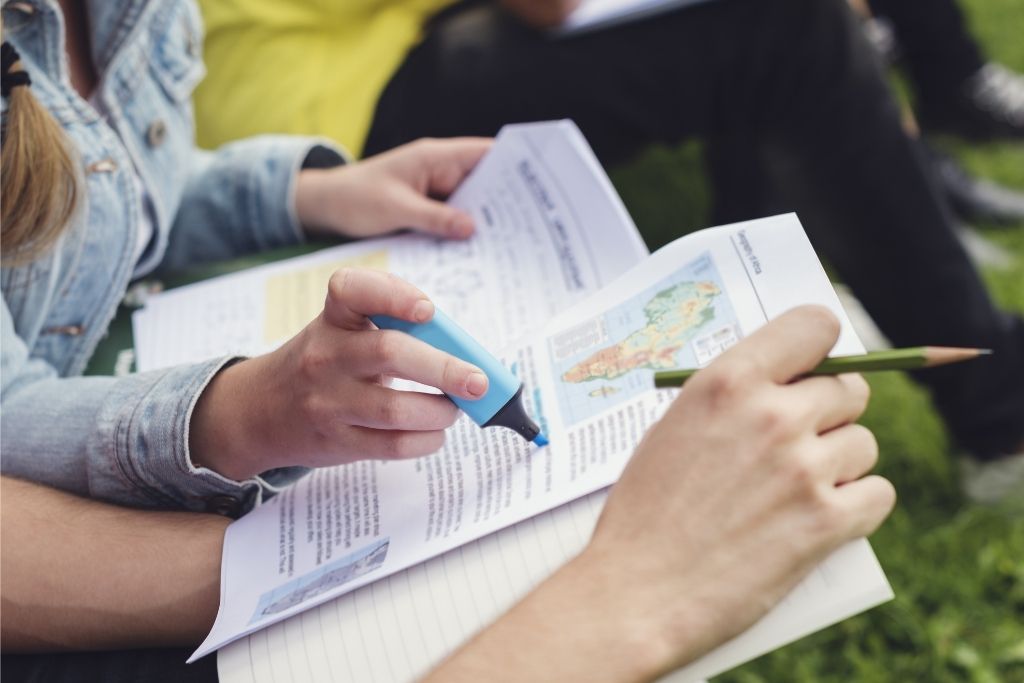 College students studying history outdoors and taking notes with a textbook