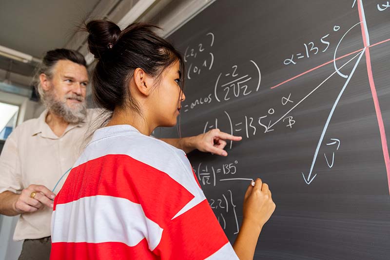 teacher helping student with math problem in blackboard