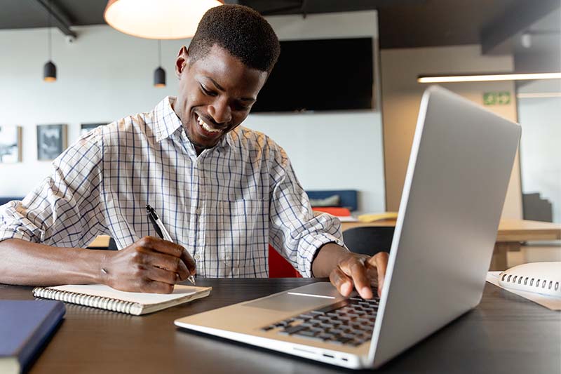 student working on laptop and writing in notebook