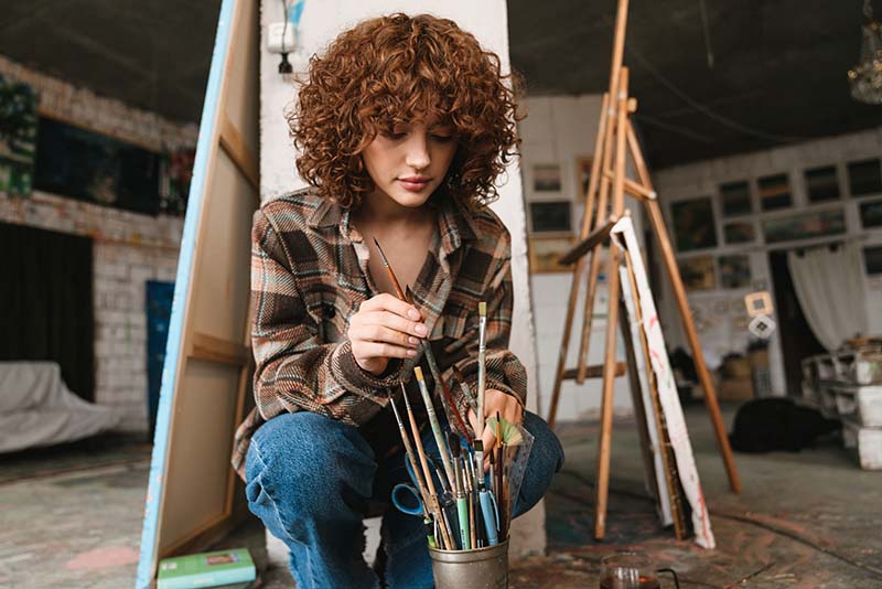 painting student choosing a brush in her studio